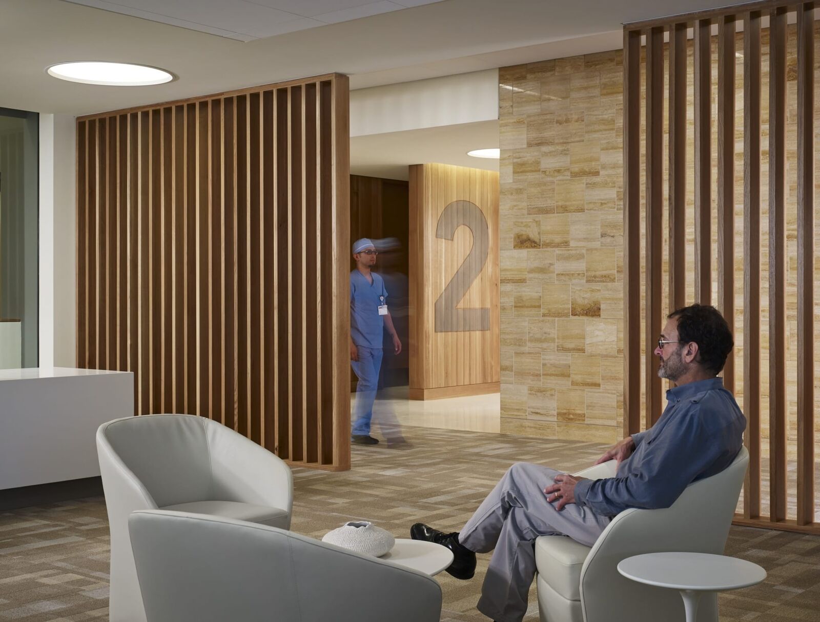 lobby area featuring man sitting by collection of chairs and man wearing hospital scrubs walking in background