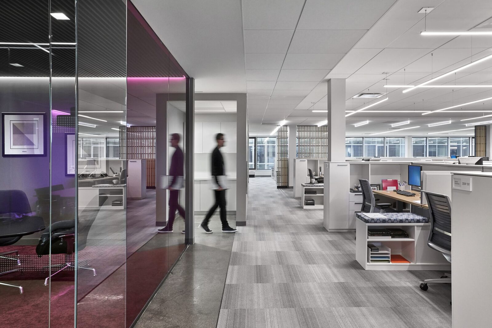Someone walks by a glass-enclosed conference room and rows of desks at the workplace