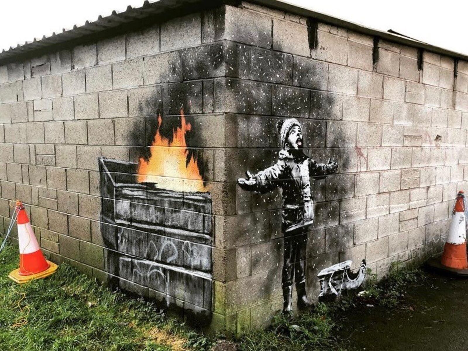 Mural of a child warming up by a dumpster fire by Banksy.