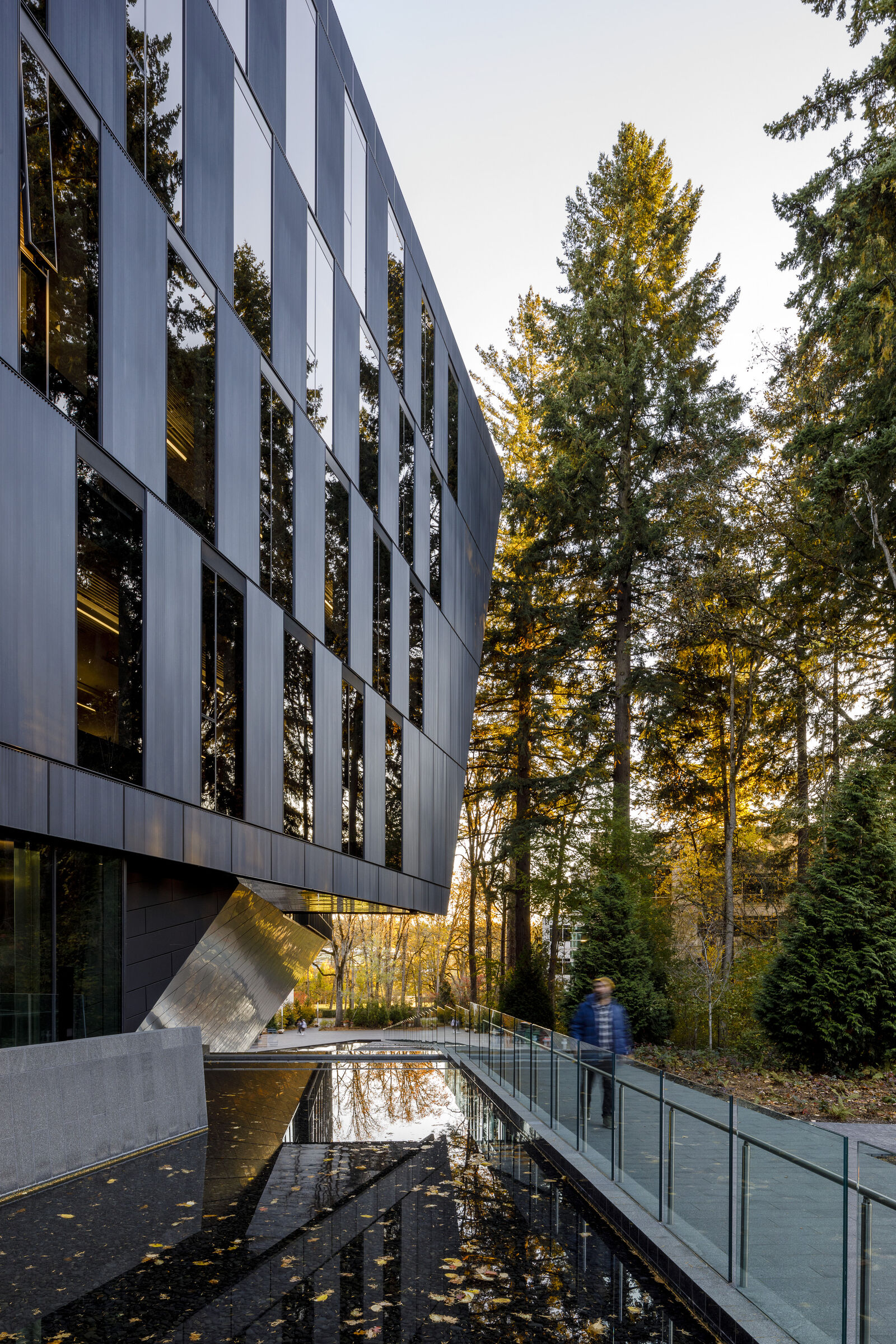 side of the building featuring windows and metal panels with person walking by pond area.