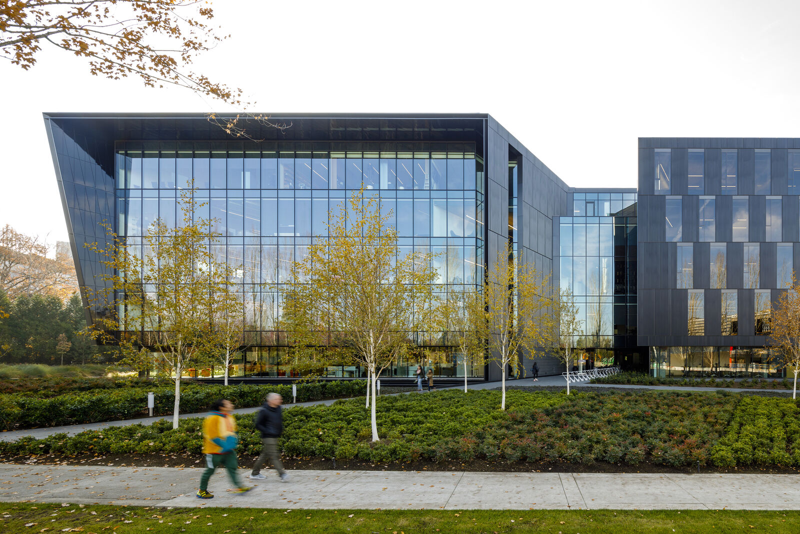 exterior of building behind garden space with people walking along sidewalk.