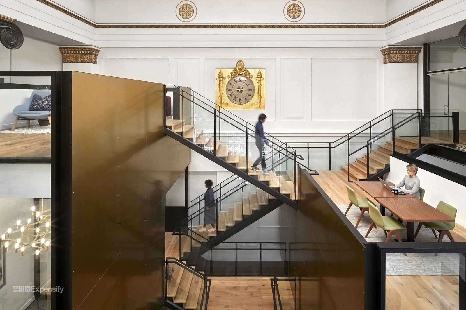 multilevel wooden staircases with people walking and women typing on laptop at table