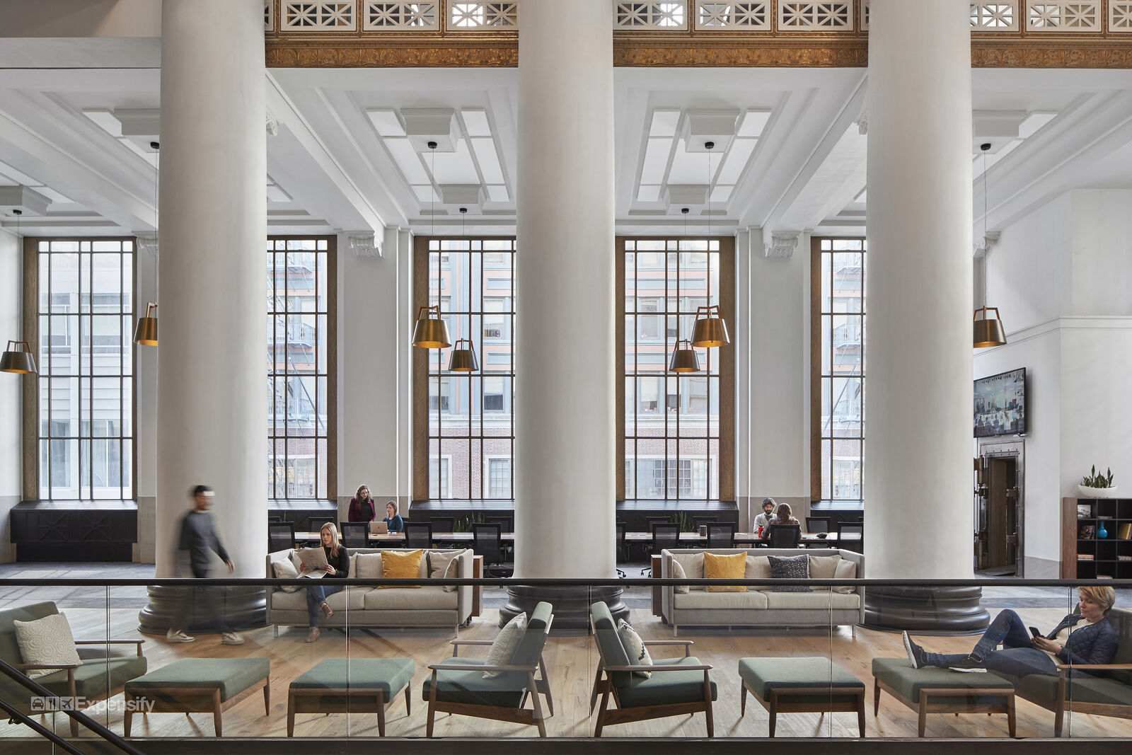 main floor with large vertical columns and various seating options with people working in different contexts. 