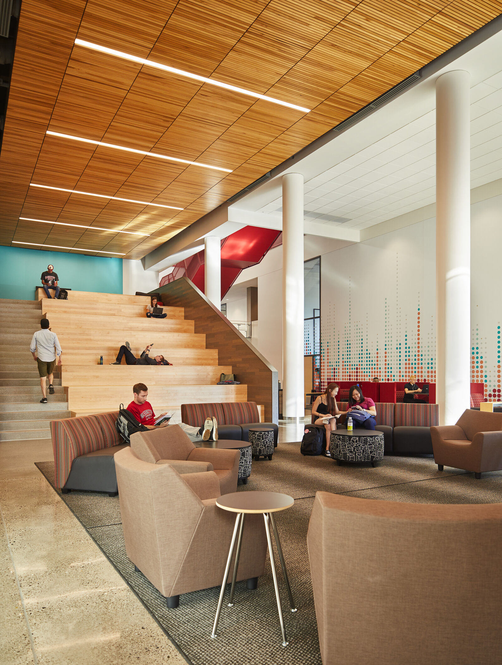 Interior photo of the grandstand wood stair with students milling around and lounge furniture on the ground level